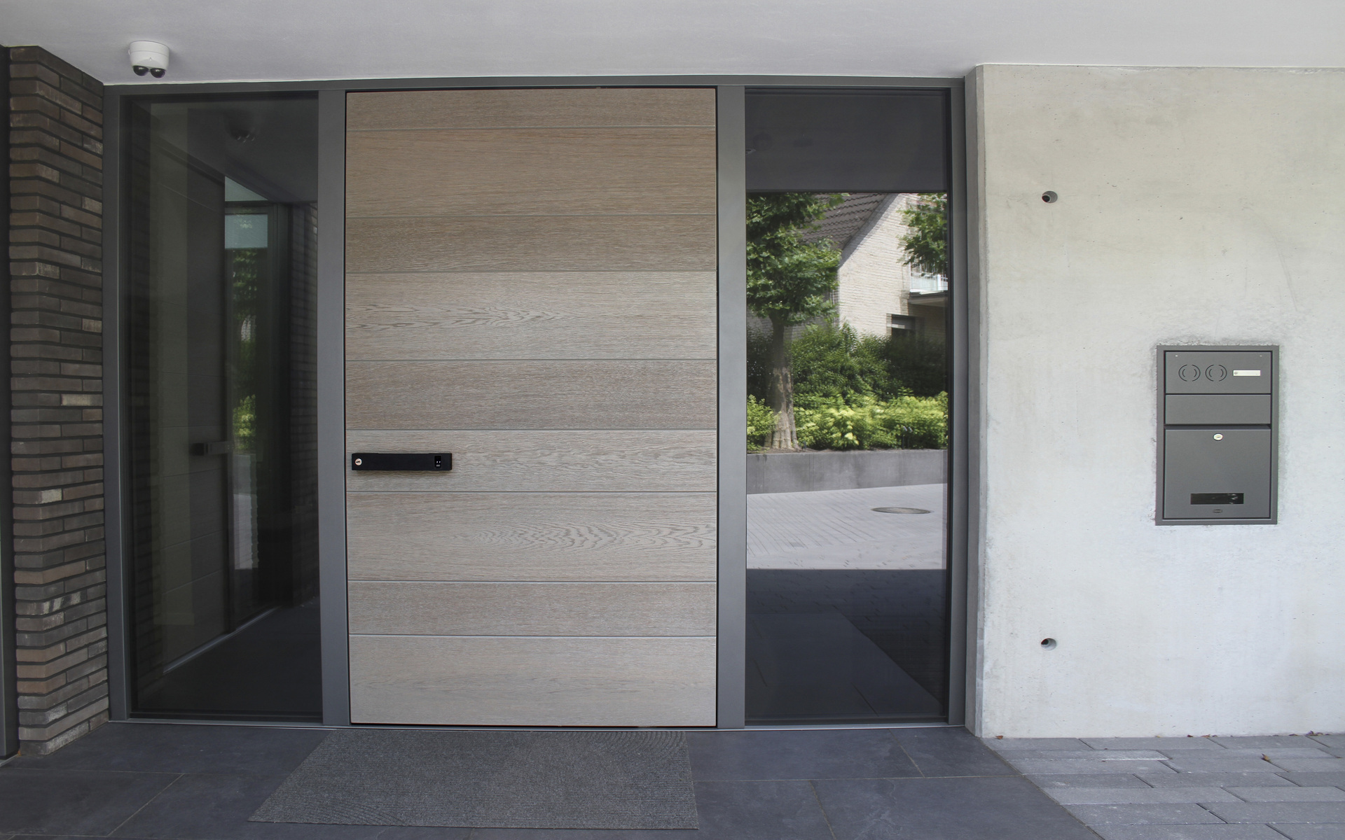 Eine moderne Eingangstür in hellem Holz mit großen Glasfenstern und Briefkasten.