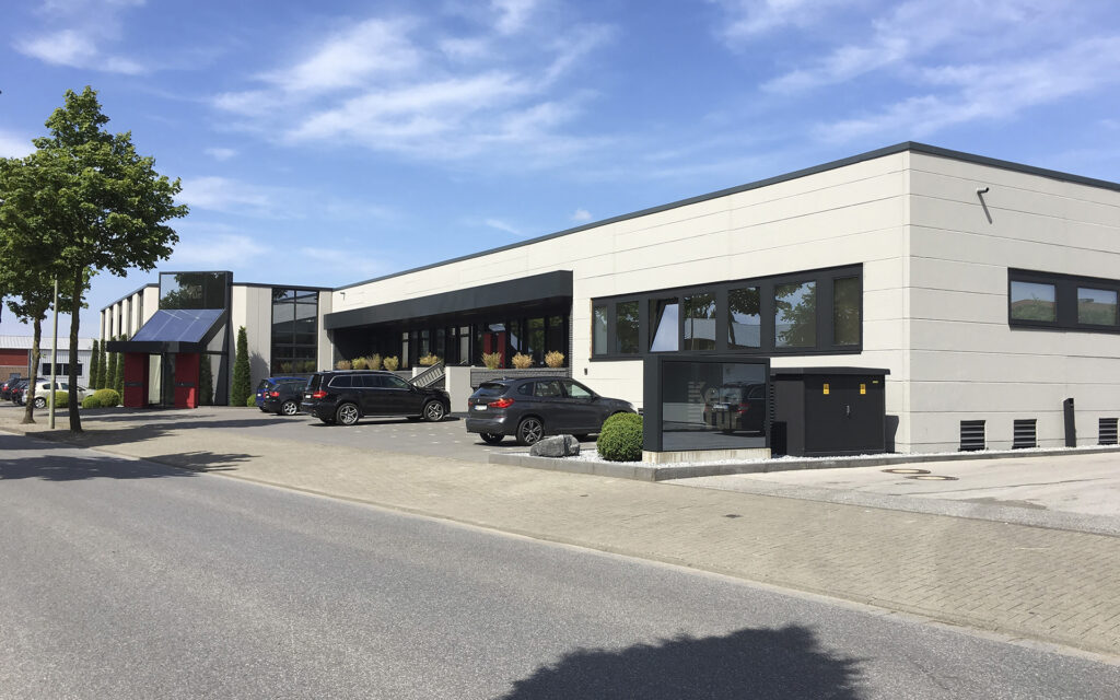 Ein modernes Bürogebäude in Beige mit mehreren Bäumen und parkenden Autos.