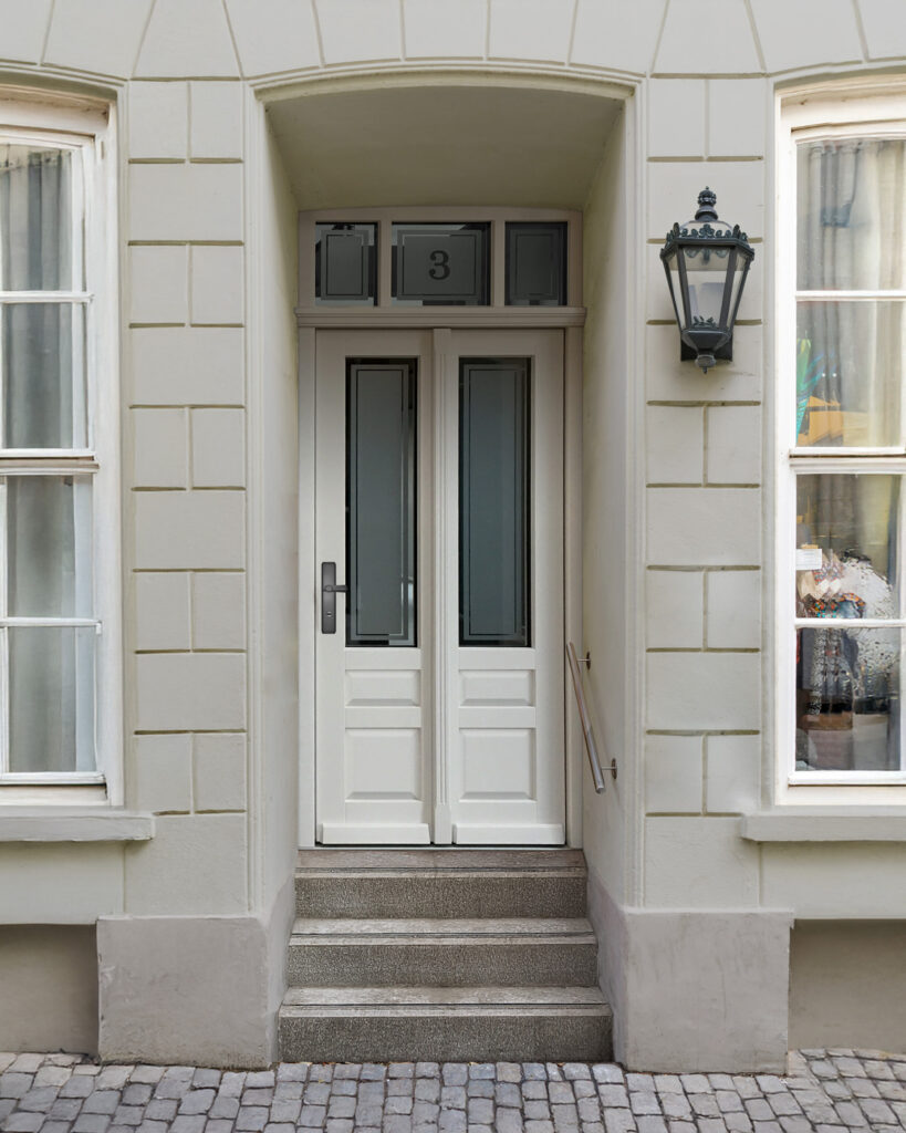 Eine weiße zweiflügelige Tür mit Stufen und Laterne an einer beigen Fassade