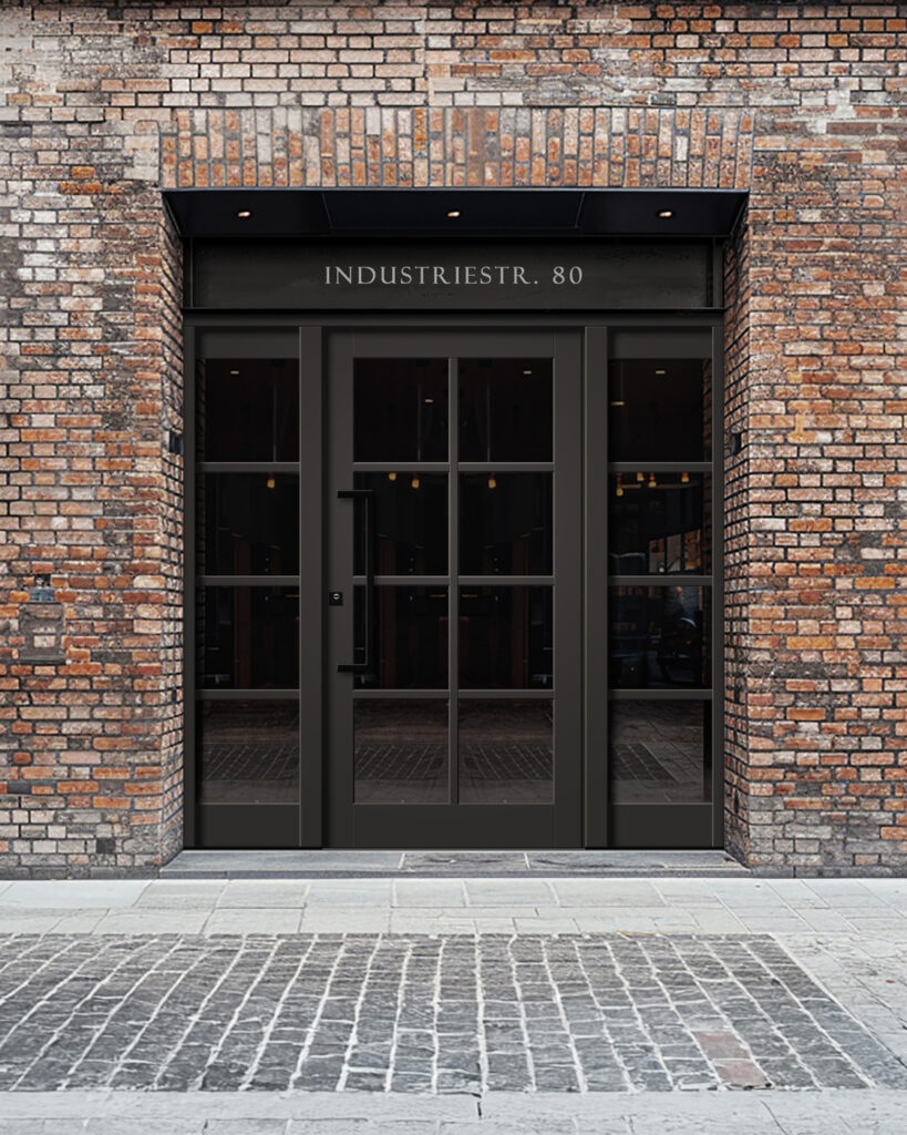 Eine moderne, schwarze Glastür mit der Aufschrift "INDUSTRIESTR. 80" in einer Ziegelmauer.