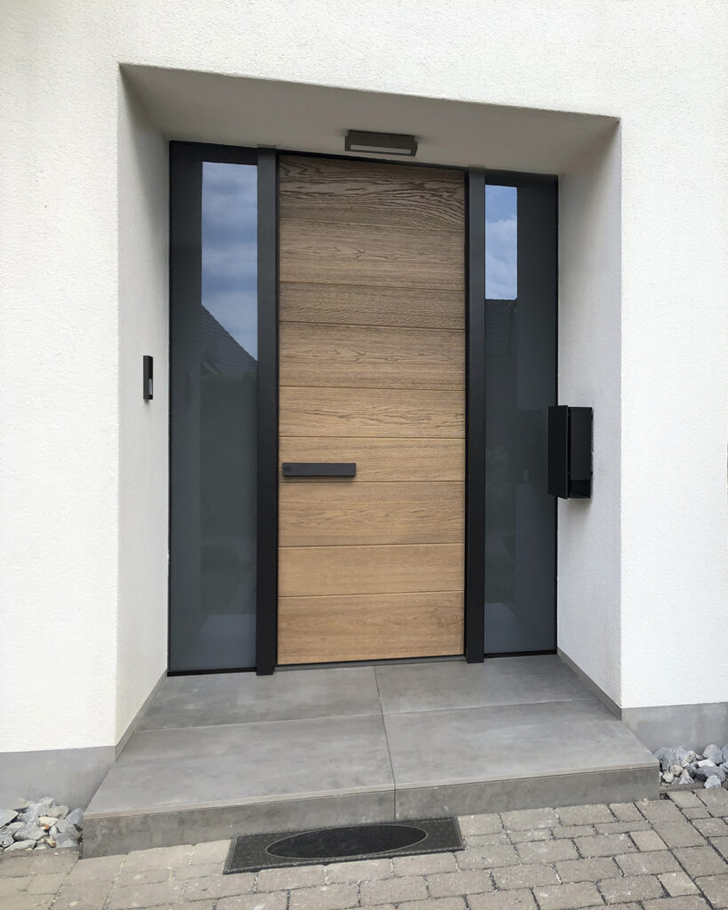Eine moderne Holztür mit seitlichen Glasfenstern in einem weißen Rahmen.