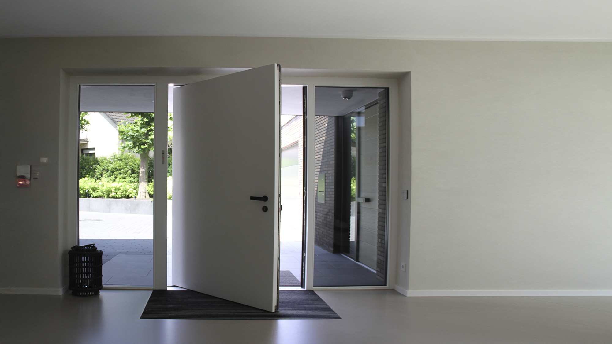 Helle Eingangshalle mit geoeffneter weisser Tuer und Glasfront ins Gruene
