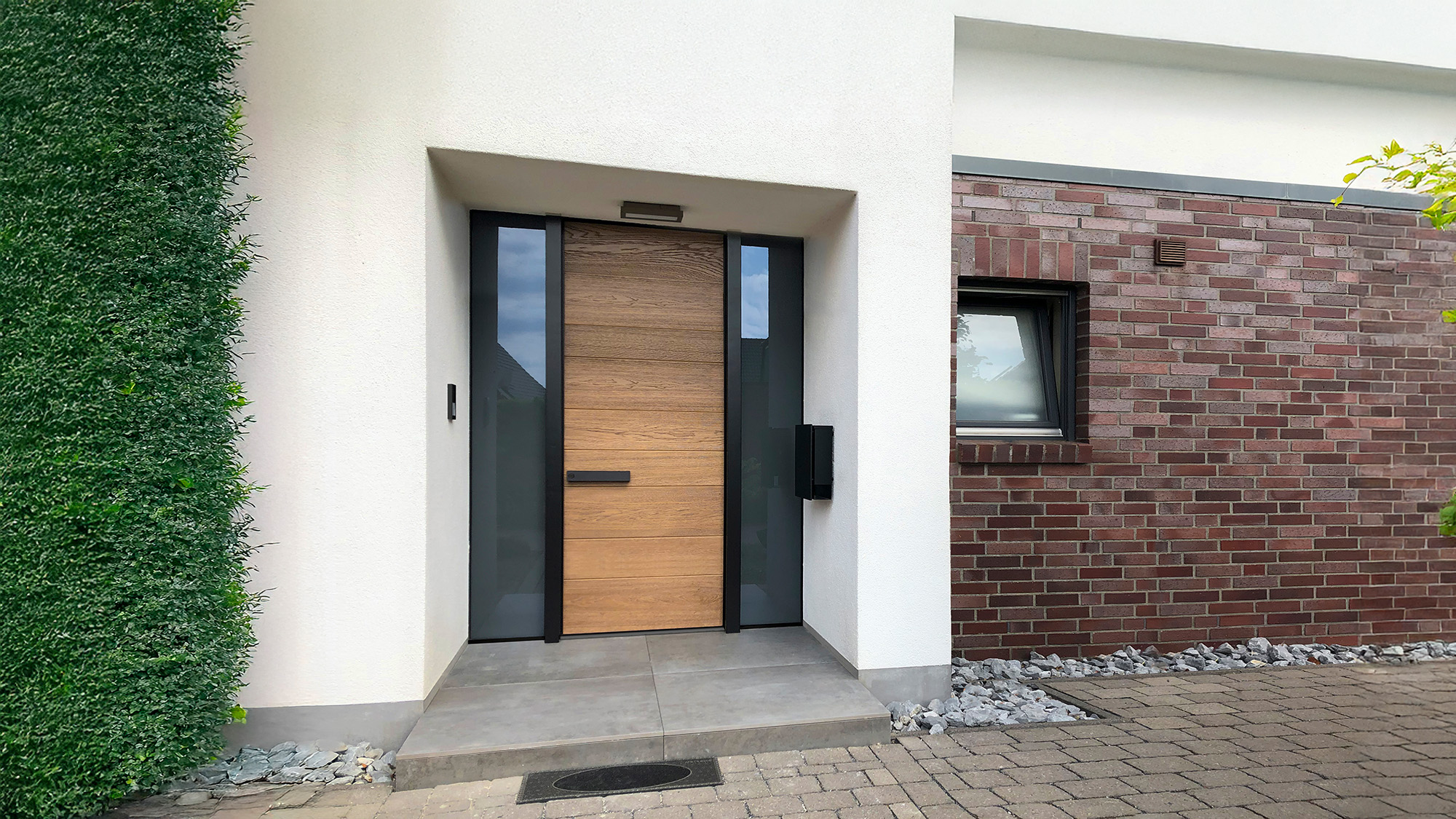 Moderne Haustuer aus hellem Holz mit Glas, umrahmt von Weiss und Klinker
